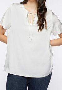 Witte blouse met korte mouwen en een relaxte pasvorm. Heeft een keyhole halslijn met strikjes en een decoratieve rand van kleine kralen nabij de halslijn.