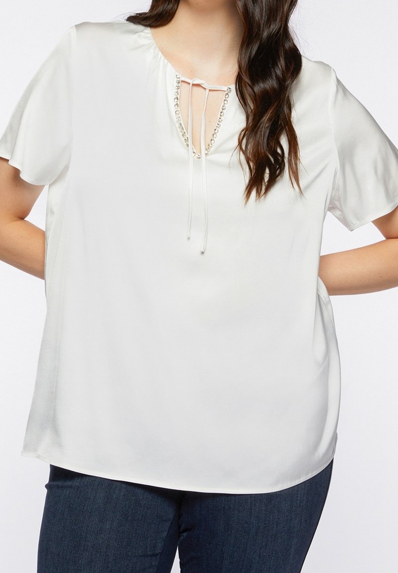 Witte blouse met korte mouwen en een relaxte pasvorm. Heeft een keyhole halslijn met strikjes en een decoratieve rand van kleine kralen nabij de halslijn.