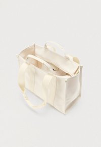 Sac cabas en toile de couleur crème avec anses doubles en tissu. Offre un intérieur spacieux et des poches zippées. Design simple avec des détails minimaux.