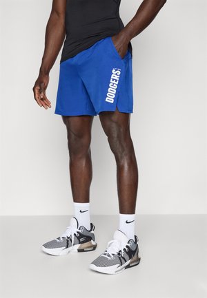 Pantaloni sportivi blu con "DODGERS" stampato in bianco sulla gamba sinistra. Indossati con sneaker bianche e nere e calzini bianchi.