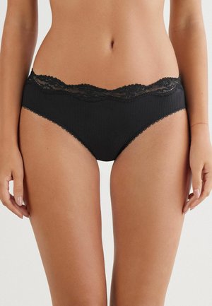 Sous-vêtements noirs côtelés avec une taille en dentelle festonnée, un subtil revêtement et une texture lisse, le tout dans un design minimaliste.