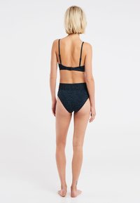 Sort bikini sæt med zebra mønster, der har en tylerem bralette og højtaljede bunde. Materialet ser glat ud med en let glans.