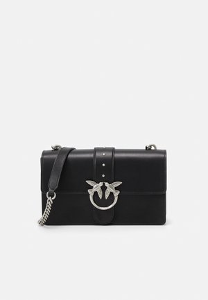 Sac bandoulière en cuir noir avec fermoir oiseau en métal argenté et détail de bandoulière chaîne sur fond blanc.