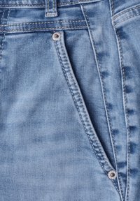 Close-up of light blue denim jeans showing front pocket, belt loop, and stitching details with metal rivets.