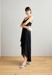 Svart asymmetrisk klänning med genomskinlig överdel, silverfärgade klackskor och en metallisk clutchväska; minimalistisk design med jämna texturer.