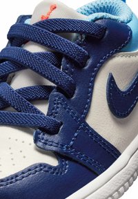 Sneaker in pelle blu navy con dettagli bianchi e azzurri. Presenta lacci in tessuto strutturato e un logo prominente sul lato. Vista ravvicinata.