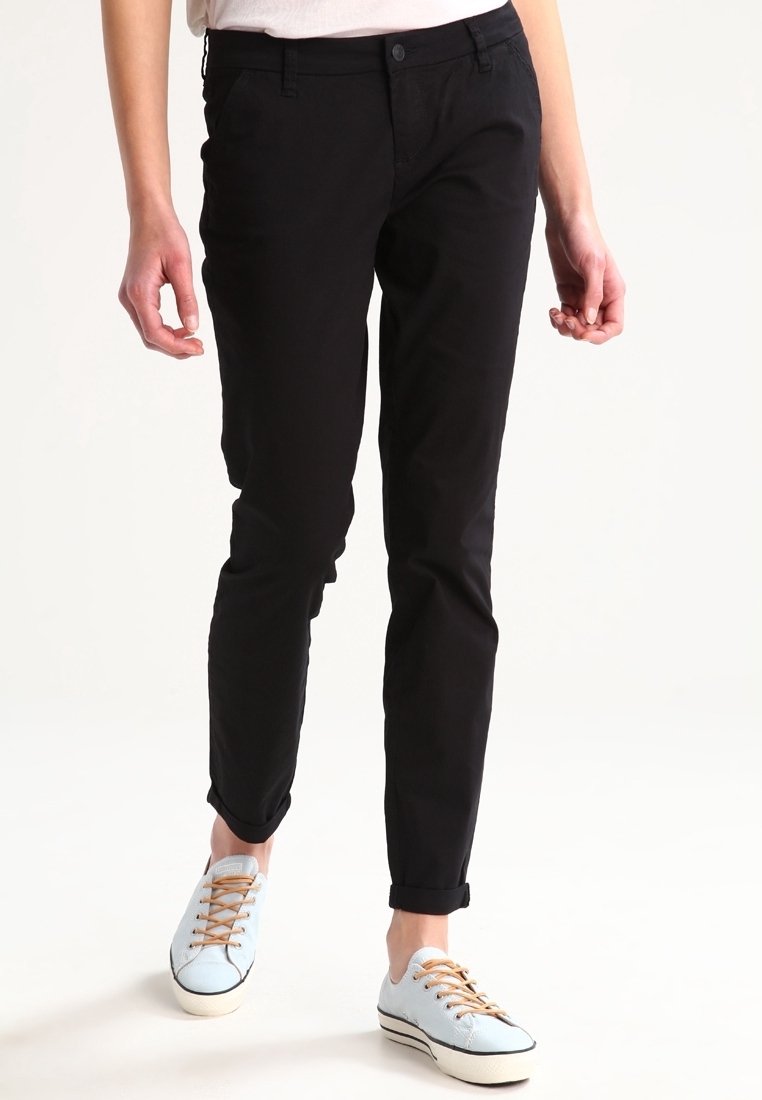 Black fitted trousers with a smooth texture, featuring side pockets and rolled-up cuffs, paired with light blue lace-up sneakers.