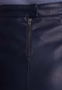 Námořnická kožená sukně s viditelným zipem na předním zapínání, s hladkou texturou a precizním prošíváním podél švů.