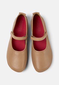 Brązowe skórzane buty typu Mary Jane z okrągłym czubkiem, pojedynczym paskiem wzdłuż podbicia oraz kontrastującą czerwoną wkładką. Gładka faktura z minimalnymi detalami.