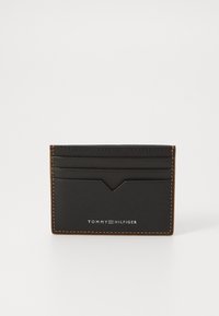 Portofel de carduri din piele neagră cu cusături portocalii, având sloturi pentru carduri și un detaliu subtil cu logo pe partea din față. Formă rectangulară, suprafață texturată.