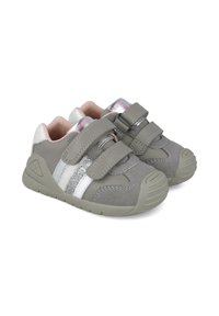 Zapatillas de deporte grises para niños pequeños, hechas de material suave, con doble tiras de Velcro, acentos plateados y suelas de goma texturizadas.