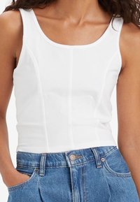 Débardeur blanc ajusté avec un décolleté carré et des détails de couture, associé à un jean en denim bleu taille haute.