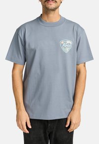 Grijze katoenen t-shirt met korte mouwen en een ronde hals. Voorzien van een kleurrijke logopatch op de linkerborst.
