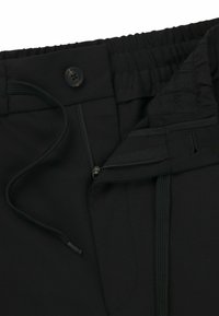 Black drawstring pants with elastic waistband, featuring a front button and a side zipper pocket. The fabric appears smooth and lightweight.
