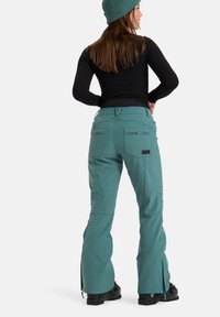 Türkise Schneehose mit taillierter Passform, mit Reißverschlusstaschen und Reißverschlüssen an den Knöcheln. Hergestellt aus wasserdichtem Material und mit gestickten Details.