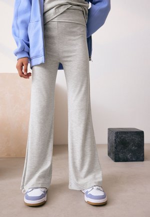 Pantaloni grigi svasati con una texture morbida, abbinati a sneakers bianche con dettagli blu. Una felpa con zip azzurra è indossata aperta.