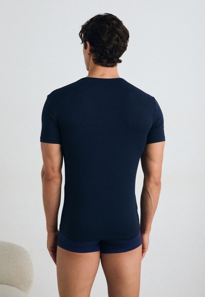 Chemise ajustée à manches courtes bleu marine, affichée de dos, fabriquée en tissu lisse, avec un col rond et des coutures minimales.