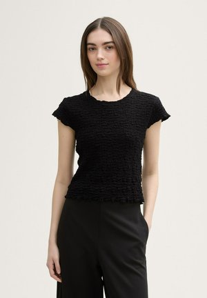 Top nero a maniche corte con un design tessuto increspato. Collo rotondo e orlo sfilacciato. Abbinato a pantaloni neri a vita alta.