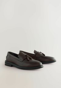 Brune læder loafers med en flad sort sål, der har en dekorativ frontrem og kvaster. Glat tekstur med subtile syningen detaljer.