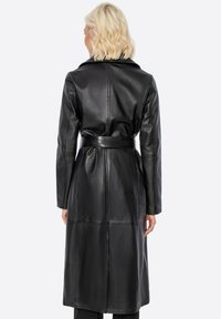 Černý kožený kabát s páskem v pase, dlouhými rukávy a klopovým límcem. Textura je hladká s lesklým povrchem.