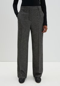 Grijze, high-waisted, wijde broek gemaakt van gestructureerde stof met voorzakken en nette stiksels. Gecombineerd met zwarte schoenen.