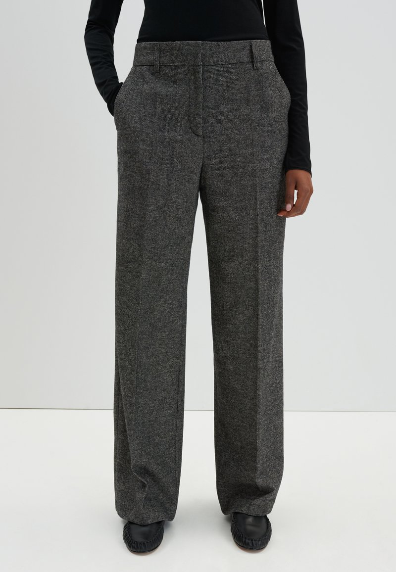 Grijze, high-waisted, wijde broek gemaakt van gestructureerde stof met voorzakken en nette stiksels. Gecombineerd met zwarte schoenen.