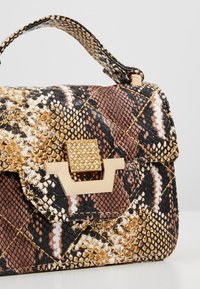 Petit sac à main avec motif peau de serpent texturé marron, noir et beige, fermoir doré avec strass incrustés, et poignée supérieure.