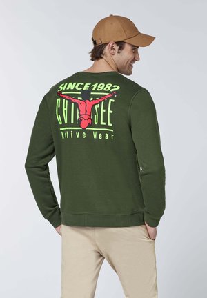 Olive green sweatshirt featuring a graphic print on the back, including text and a design in bright colors. Long sleeves and ribbed cuffs.