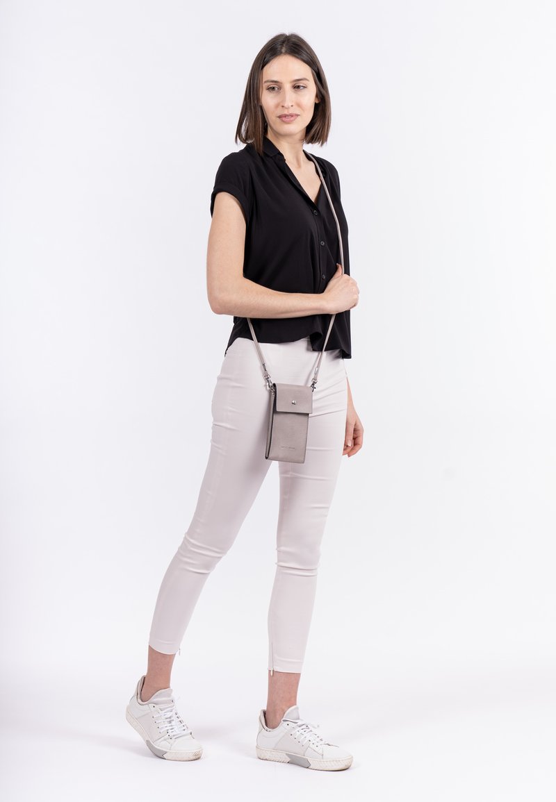 Camisa negra de botones de manga corta, pantalones ajustados gris claro y zapatillas blancas. Bolso cruzado gris con solapa y correa.