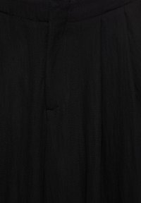 Pantalon en tissu noir en gros plan montrant la ceinture, la couture et les détails de la poche.