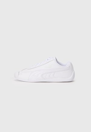 Biały niski sneaker Puma z naszywanym paskiem z logo, wiązany sznurówkami i gumową podeszwą, pokazany z boku na jasnym tle.