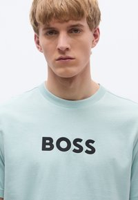 Helehall sinine puuvillane T-särk ümar kaelusega ja ees musta "BOSS" logoga, millel on lühikesed varrukad ja pehme tekstuur.