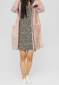 Veste de pluie légère et translucide rose avec une robe noire à motifs floraux en dessous. Comprend de grandes poches et des baskets blanches.