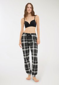 Reggiseno nero abbinato a pantaloni da pigiama a quadri bianchi e neri. I pantaloni presentano un elastico in vita e alle caviglie con un cordino.
