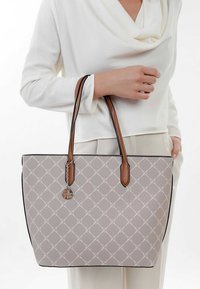 Světle šedá taška na rameno s vyraženým diamantovým vzorem, černým lemováním a hnědými koženými uchy. Na straně je připevněn stříbrný přívěsek.