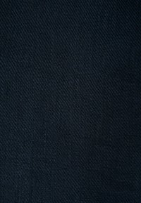 Gros plan sur un tissu noir texturé montrant un motif tissé serré et des lignes diagonales dans le matériau.