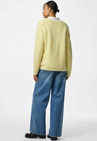 Gul fluffig tröja med vid passform och låg bakflik; kombinerat med löst sittande blå denimjeans och svarta plattformstövlar.