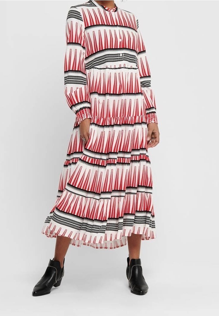 Robe à manches longues à motifs rouges, noirs et blancs, avec des volants en étages et un col rond, associée à des bottines noires.