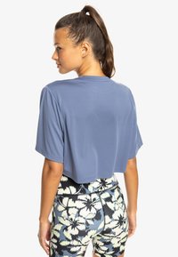 Cropped short-sleeve top in blue fabric, smooth texture. Paired with patterned leggings featuring floral designs in blue, white, and black.