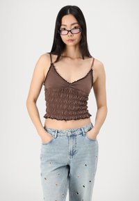 Brun cropped tank top med volanger på kantene og smocket tekstur, kombinert med lyseblå denimjeans med sirkelutskjæringer.