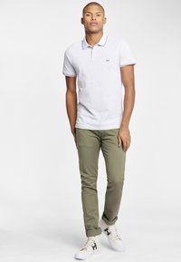 Lysegrå polo T-shirt med kontrasterende krave accenter, parret med olivengrønne slim-fit bukser og hvide sneakers. Rent og moderne design.