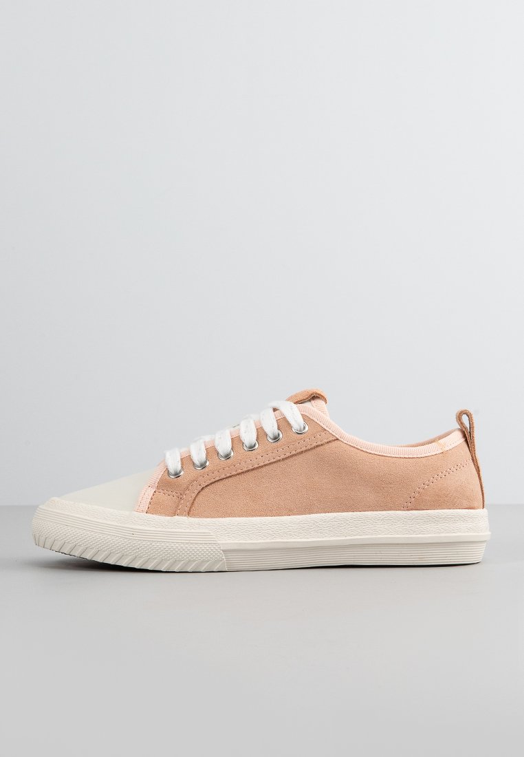 Zapatilla de ante rosa claro con puntera y suela de goma blanca, con cordones blancos y un lazo en el talón para facilitar su uso.