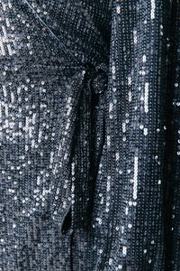 Crni sequin materijal s detaljem vezanja. Površina sadrži brojne sjajne, okrugle sekvine, stvarajući teksturirani, sjajni efekt.