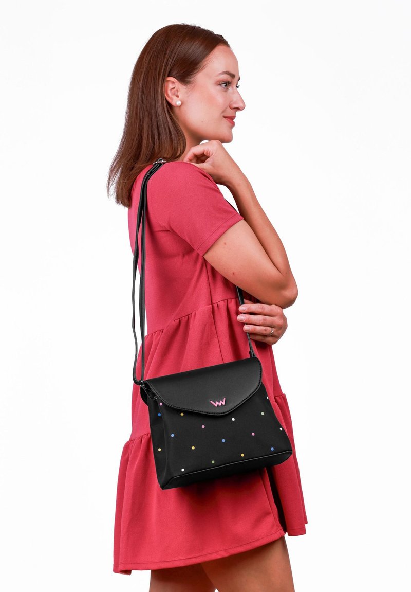 Černá kožená taška přes rameno s barevnými puntíky, s klopou na zavírání a nastavitelným popruhem. Na přední části se nachází logo.
