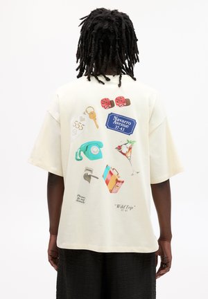 Krèmfarvet oversized t-shirt med forskellige farverige grafikker, herunder en nøgle, telefon, drink, kuffert og tekst accenter på ryggen.