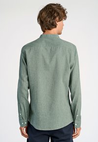 Camisa verde de manga larga con un tejido sutilmente texturizado, puños de botón y un cuello clásico, vista desde la parte de atrás.