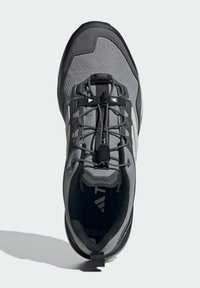 Scarpa sportiva grigia con tomaia in mesh testurizzato, accenti neri, lacci elastici e suola in gomma. Presenta un pratico passante sul tallone.
