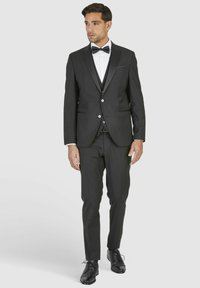 Zwarte tuxedo met satijnen revers, slim-fit ontwerp, enkel uitgevoerd, gecombineerd met een wit hemd en een zwarte vlinderdas. Glanzende zwarte wettelijke schoenen.