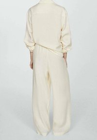 Crème-kleurige, losse blouse met opgerolde mouwen en bijpassende wijde broek. Zacht materiaal met een gladde textuur, minimale details.