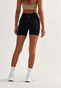 Black athletic shorts with a tight fit and a mid-rise waist, paired with white sneakers and light-colored socks featuring a logo.